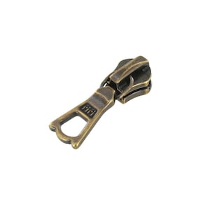 May include: A gold-toned metal zipper pull with a small, open loop on the bottom and the word "Riri" engraved on the side.