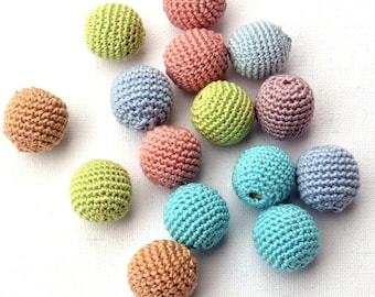 May include: A collection of 13 crocheted balls in various pastel colors, including light blue, pink, green, and beige. The balls are arranged in a loose pile on a white surface.