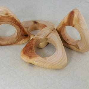 May include: Three wooden napkin rings in the shape of a triangle with a circular opening in the center. The rings are made of light brown wood with a natural grain pattern.