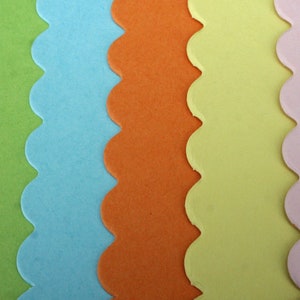 May include: Five vertical strips of paper with scalloped edges arranged side by side. The colors from left to right are lime green, light blue, bright orange, pale yellow, and soft pastel pink. Each strip features a smooth, matte finish.