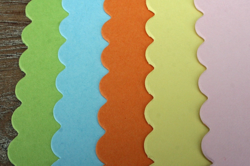 May include: Five vertical strips of paper with scalloped edges arranged side by side. The colors from left to right are lime green, light blue, bright orange, pale yellow, and soft pastel pink. Each strip features a smooth, matte finish.