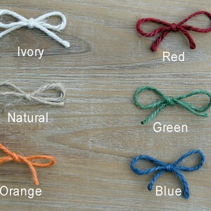 May include: Six different colors of twine tied into bows. The colors are ivory, red, natural, green, orange, and blue.