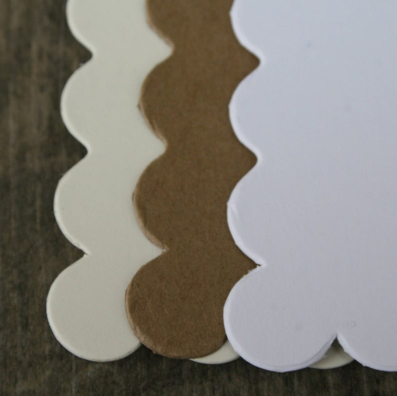May include: Three scalloped-edge paper tags or labels arranged in a vertical stack. The top layer is bright white, the middle layer is a natural brown kraft paper, and the bottom layer is a light cream color. Each piece has a smooth, rounded edge.