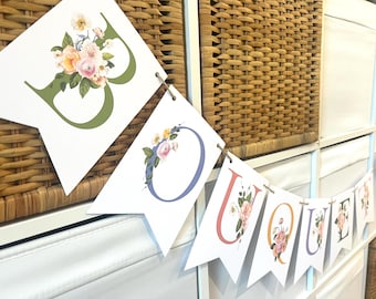 May include: A white banner with the word "BOUQUET" spelled out in colorful letters. Each letter is decorated with a floral design and a small cluster of flowers.