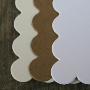 May include: Three scalloped edge paper squares, one white, one brown, and one white. The squares are stacked on top of each other.