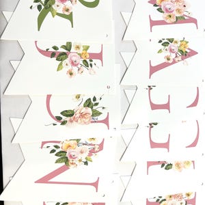 May include: A pink and green floral banner with the word "WELCOME" spelled out in pink letters. Each letter is decorated with a floral arrangement of pink, yellow, and white flowers.