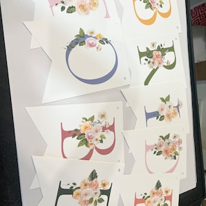 May include: A floral banner with the word "Birthday" spelled out in different colors. Each letter is decorated with a floral arrangement in shades of pink, yellow, and green.