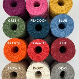 K&ouml;nnte beinhalten: Zw&ouml;lf Spulen Garn in verschiedenen Farben, darunter Orchidee, Rosa, Gold, Gr&uuml;n, Pfau, Blau, Orange, Tomate, Rot, Braun, Elfenbein und Grau.