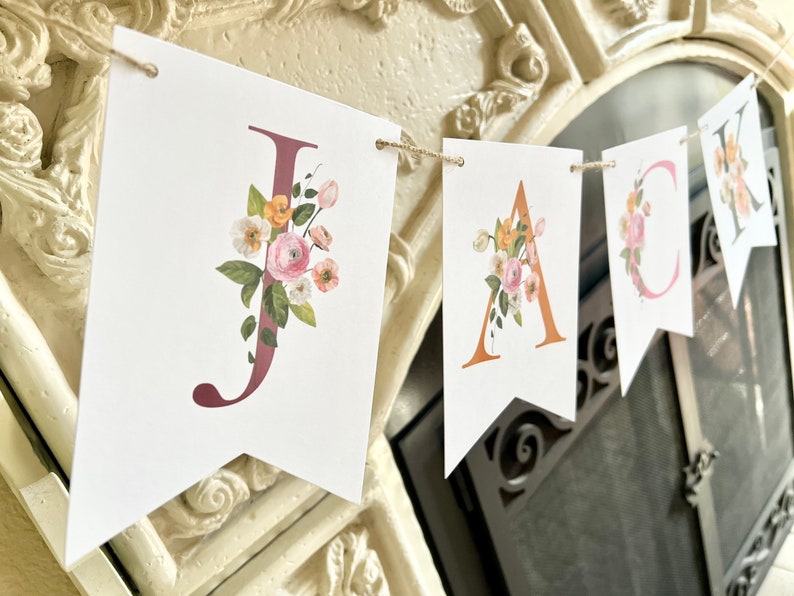 May include: A floral banner with the name "JACK" spelled out in individual flags. Each letter is decorated with pink, yellow, and green watercolor flowers.