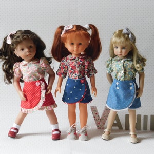 Peut inclure: Trois poupées portant des chemisiers à imprimé floral et des jupes de couleurs différentes. La poupée de gauche porte une jupe rouge à pois blancs et une bordure de dentelle blanche. La poupée du milieu porte une jupe en jean bleu avec des cœurs blancs et une bordure de dentelle blanche. La poupée de droite porte une jupe en jean bleu à pois blancs et une bordure de dentelle blanche.