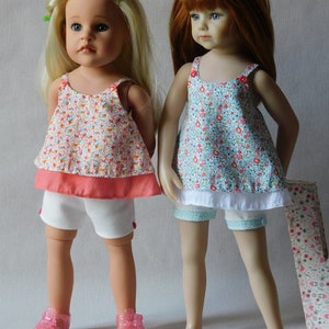 以下が含まれることがあります： 夏服を着た人形が2体。左の人形はピンクと白の花柄のドレスに白いペチコートと白いショートパンツを履いています。右の人形は青と白の花柄のドレスに白いペチコートと白いショートパンツを履いています。2体とも長い髪で、サンダルを履いています。