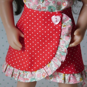 May include: A red skirt with white polka dots and a floral ruffle trim. The skirt is wrapped and has a pink heart-shaped button.