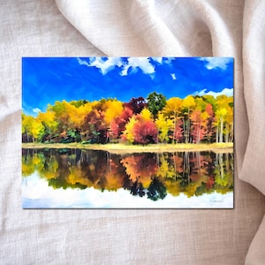 May include: A vibrant landscape painting depicts a colorful autumn scene. The artwork showcases a forest with trees in shades of yellow, red, and orange reflected in a calm body of water under a bright blue sky with fluffy white clouds.