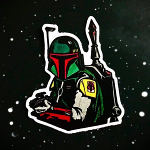 May include: A green and red Boba Fett character sticker with a white outline. The sticker is set against a black background with white dots.