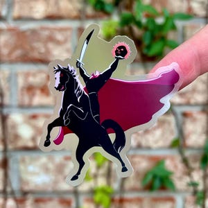 Puede incluir: Una pegatina transparente con una silueta negra de un jinete sin cabeza sobre un caballo negro encabritado. El jinete sostiene una espada y una calavera en llamas. La pegatina tiene una capa roja y un fondo verde claro.