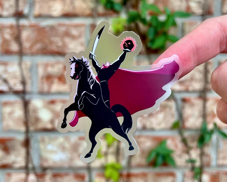 Puede incluir: Una pegatina transparente con una silueta negra de un jinete sin cabeza sobre un caballo negro encabritado. El jinete sostiene una espada y una calavera en llamas. La pegatina tiene una capa roja y un fondo verde claro.