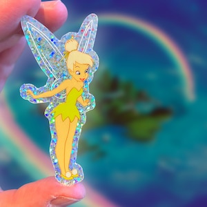 K&ouml;nnte beinhalten: Ein transparenter Aufkleber mit Glitzer-Finish, der Tinkerbell zeigt, eine Fee mit gr&uuml;nen Fl&uuml;geln und einem gr&uuml;nen Kleid, die auf einem blauen und gr&uuml;nen Hintergrund steht.
