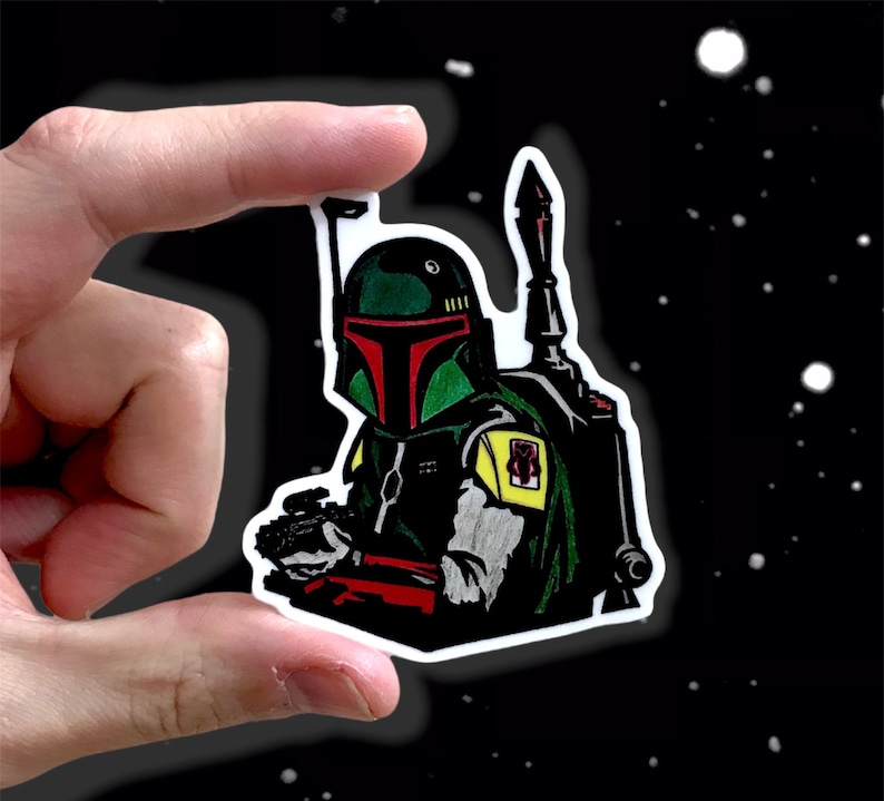 May include: A green and black Star Wars Boba Fett sticker with a yellow and red design. The sticker features a detailed illustration of Boba Fett's helmet and armor.