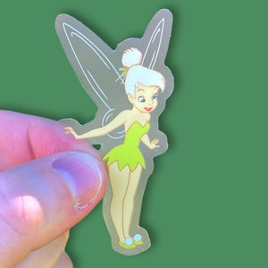 K&ouml;nnte beinhalten: Ein transparenter Aufkleber mit Tinkerbell, einer Fee mit gr&uuml;nen Fl&uuml;geln und einem gr&uuml;nen Kleid. Sie hat blonde Haare und l&auml;chelt.