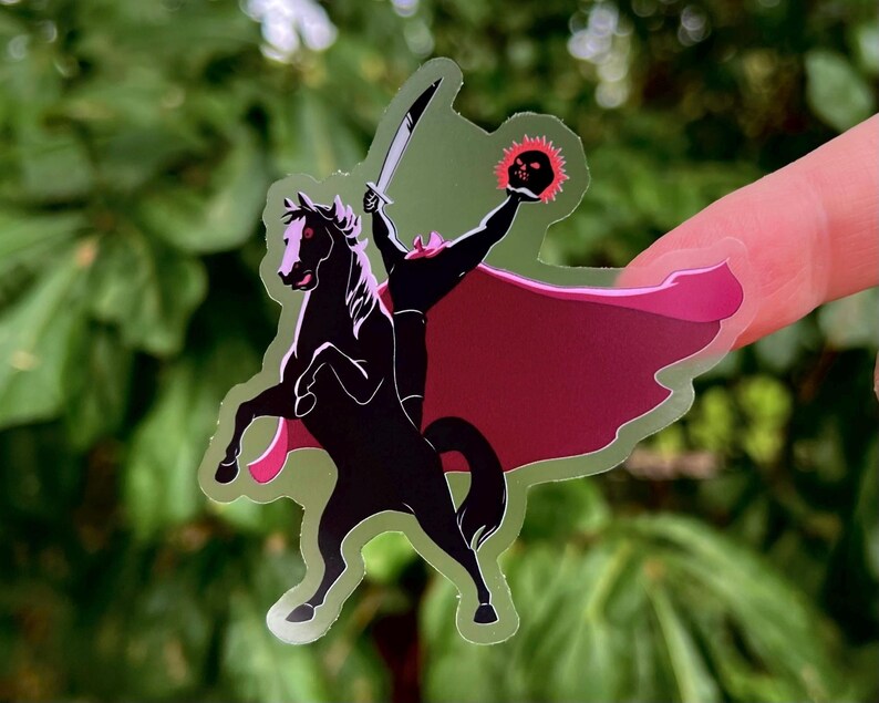Puede incluir: Una pegatina transparente con un caballo negro encabritado con un jinete sin cabeza sosteniendo una espada y una linterna de calabaza en llamas. El jinete lleva una capa roja. La pegatina tiene un contorno verde.