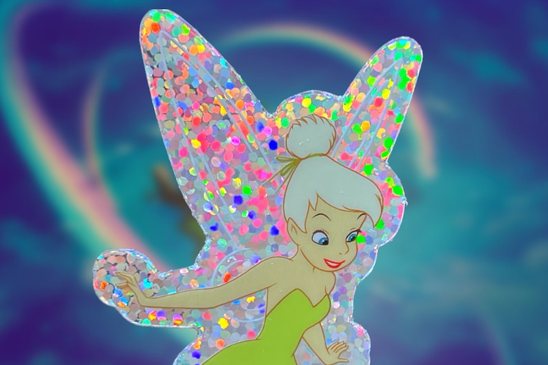 K&ouml;nnte beinhalten: Ein glitzernder, regenbogenfarbener Aufkleber von Tinkerbell, einer Fee mit gr&uuml;nen Fl&uuml;geln und einem gr&uuml;nen Kleid, vor einem blauen und violetten Hintergrund.