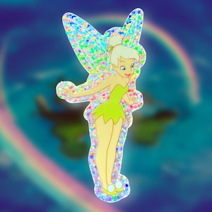 K&ouml;nnte beinhalten: Ein glitzernder, regenbogenfarbener Aufkleber mit Tinkerbell, einer Fee mit gr&uuml;nen Fl&uuml;geln und einem gr&uuml;nen Kleid, vor einem blauen und violetten Hintergrund.