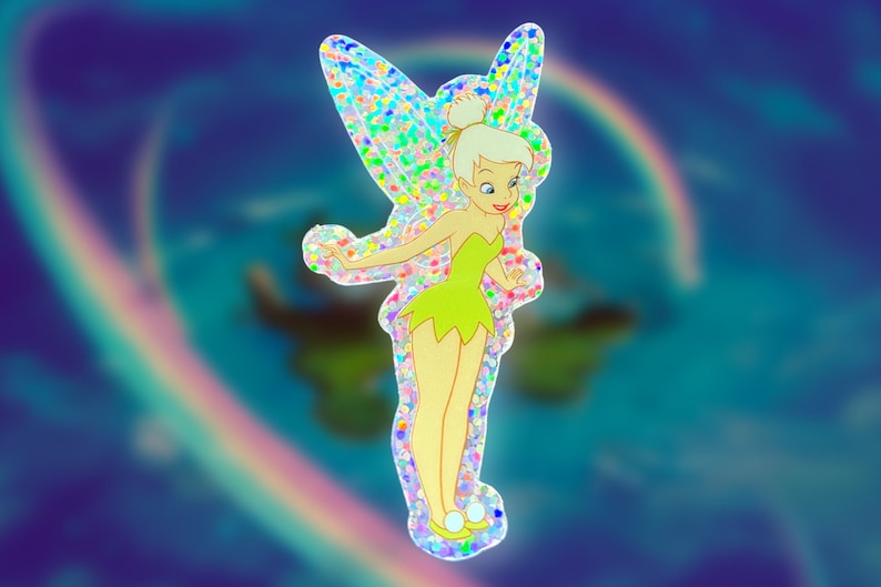 K&ouml;nnte beinhalten: Ein glitzernder, regenbogenfarbener Aufkleber mit Tinkerbell, einer Fee mit gr&uuml;nen Fl&uuml;geln und einem gr&uuml;nen Kleid, vor einem blauen und violetten Hintergrund.