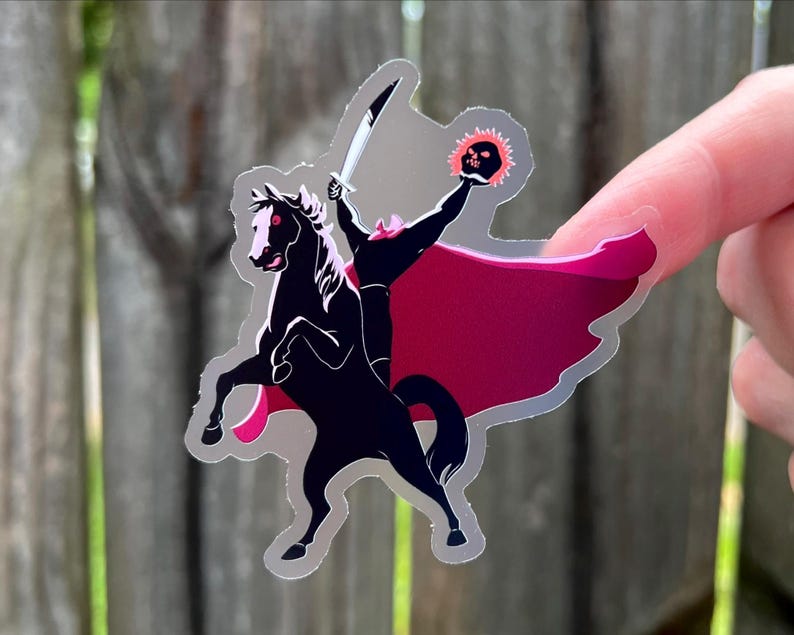 Puede incluir: Una pegatina que representa a un jinete sin cabeza montado en un caballo negro encabritado. El jinete empu&ntilde;a una espada y una calavera en llamas. La pegatina tiene una capa roja y rosa y un contorno plateado. El dise&ntilde;o est&aacute; inspirado en el cuento cl&aacute;sico.