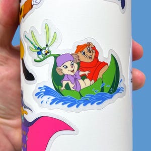 May include: A white sticker with a cartoon image of two mice in a green boat on blue water. The mice are wearing purple and red clothing. A green dragonfly is in the background.