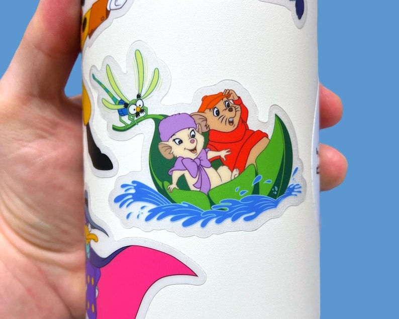 May include: A white sticker with a cartoon image of two mice in a green boat on blue water. The mice are wearing purple and red clothing. A green dragonfly is in the background.
