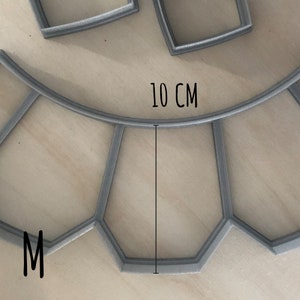 May include: A gray metal mold with a 10 cm diameter, shaped like a circle with a section cut out. The mold is labeled with the letter "M".
