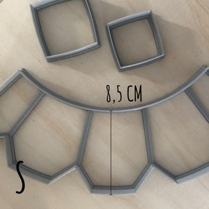 May include: A gray plastic cookie cutter shaped like a window with 8.5 inches in diameter. The cutter has a curved top and a straight bottom. There are two smaller square cookie cutters in the background.