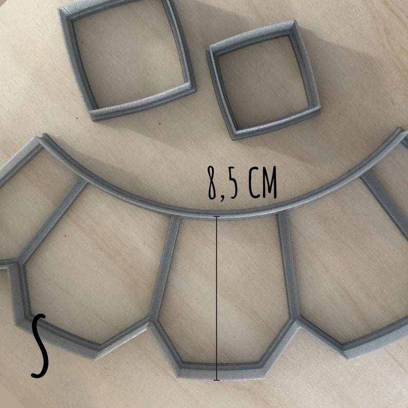 May include: A gray plastic cookie cutter shaped like a window with 8.5 inches in diameter. The cutter has a curved top and a straight bottom. There are two smaller square cookie cutters in the background.