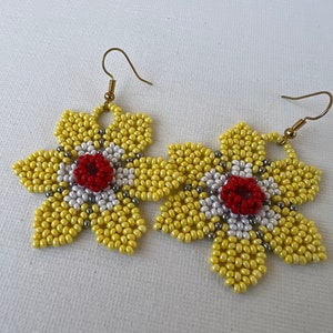 Peut inclure: Une paire de boucles d'oreilles en forme de fleur jaune avec des centres rouge et blanc. Les boucles d'oreilles sont faites de petites perles et ont des crochets dorés.