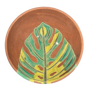 May include: A terracotta bowl with a green and yellow leaf design. The bowl is perfect for serving snacks or dips.