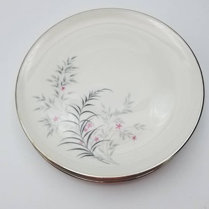 May include: A set of three white ceramic dinner plates with a silver rim. The plates feature a floral design with pink flowers and gray leaves.