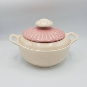 May include: A white ceramic casserole dish with a pink lid. The lid has a fluted edge and a small knob on top. The dish has two handles.