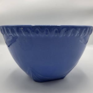 May include: A light blue ceramic mixing bowl with a scalloped rim and a decorative design. The bowl is made of a smooth, glazed ceramic.