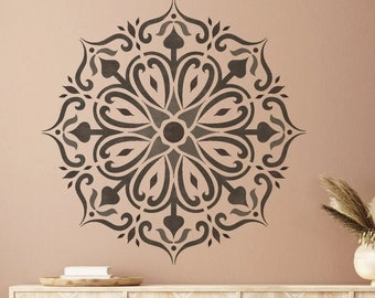 May include: A brown leather pouf ottoman sits in front of a wooden cabinet with a white painted surface and a stencil design. The cabinet has three doors and is decorated with a large mandala stencil design on the wall behind it.