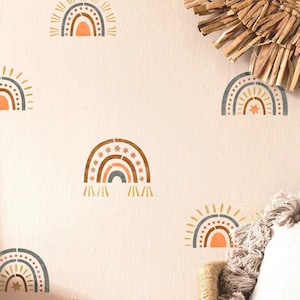 Peut inclure: Des autocollants muraux en forme d'arc-en-ciel dans des tons de marron, orange et gris, avec des détails d'étoiles et de soleil. Ils sont disposés sur un mur beige clair, pour une décoration de chambre d'enfant ou de salle de jeux.