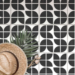 May include: A repeating black and white geometric tile pattern. A straw hat, green palm leaf, and dried seed pods are arranged in the foreground. The tiles have a semi-gloss finish, creating a modern aesthetic. The design is reminiscent of mid-century modern style.