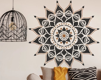 May include: A wooden couch with a beige cushion and a yellow throw blanket. The couch is in front of a white wall with a black and brown mandala painted on it. There is a black wicker pendant light hanging above the couch.