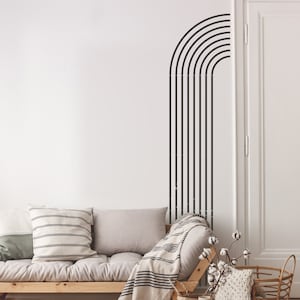 May include: A white wall with a black geometric design of curved lines. A light brown sofa with a white and black striped throw blanket is in the foreground.