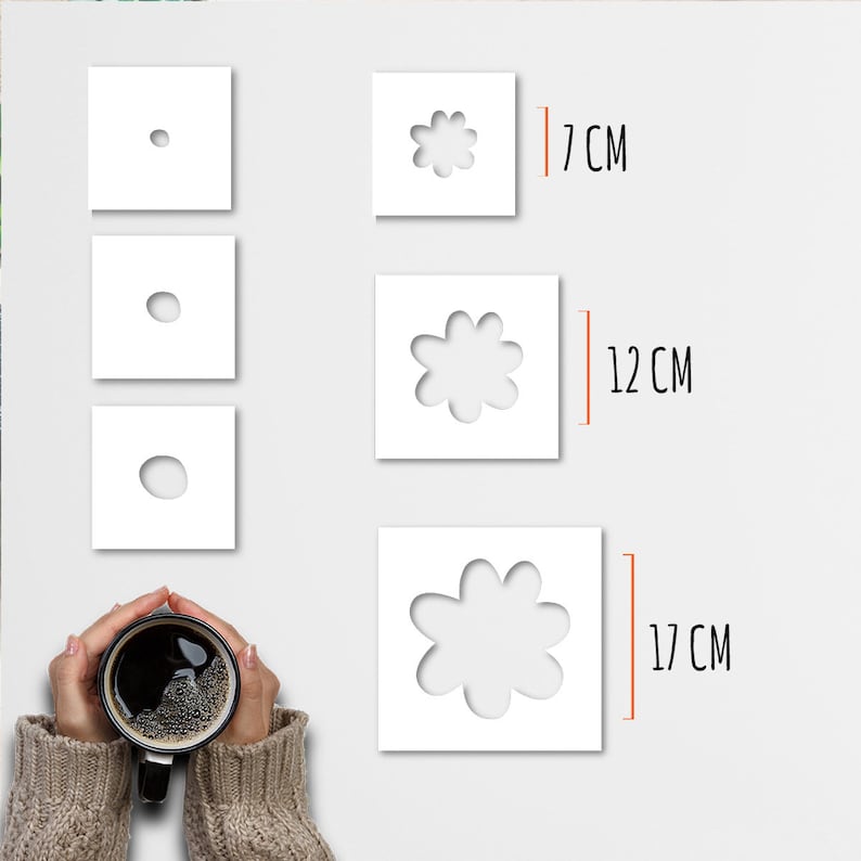 May include: White square stencils with flower cutouts in three sizes: 7 cm, 12 cm, and 17 cm. Three smaller squares show the progression of the flower's center. A person holds a black mug of coffee.
