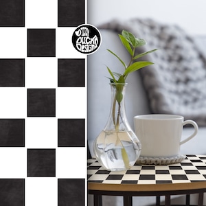 Könnte beinhalten: Eine schwarz-weiße Schachbrett-Tischplatte mit einer weißen Tasse und einer durchsichtigen Glasvase mit grünen Stielen und Blättern. Die Tischplatte ist aus Holz und hat ein schwarz-weißes Schachbrettmuster. Die Tasse ist weiß und hat einen abgerundeten Griff. Die Vase ist aus klarem Glas und hat einen abgerundeten Boden. Die Stiele und Blätter sind grün und in einem einfachen Muster angeordnet.