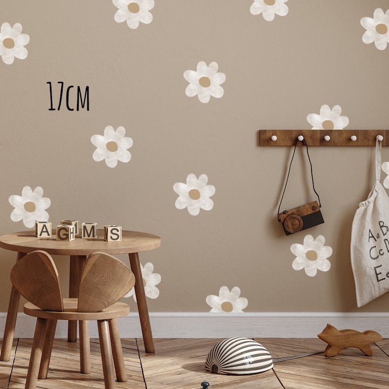 May include: A room decorated with daisy flower wall decals. The daisies are white with a tan centre. A wooden table and chair are in the foreground. A wooden camera and bag hang on the wall. The text "17cm" is visible.