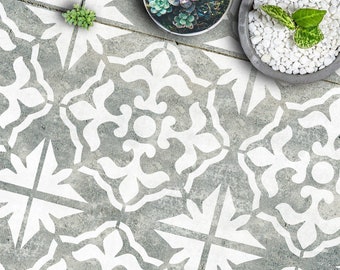 May include: A gray concrete floor with a white stencil design of repeating geometric shapes. The floor is decorated with two small potted plants.