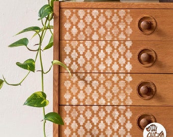 May include: A wooden dresser with four drawers, painted with a white geometric pattern. The pattern is a repeating design of diamonds and squares. The dresser has round wooden knobs on each drawer.