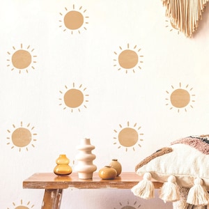 May include: A white wall with a pattern of brown sun decals. There are three vases on a wooden table in front of the wall. The vases are brown, white, and beige.