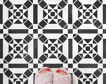 May include: A pair of pink fuzzy slippers with red nail polish on the toes. The slippers are on a black and white geometric patterned floor.